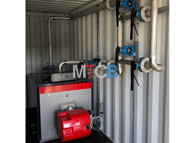 Photographie de l'intérieur d'une chaufferie mobile préfabriquée contenant une chaudière eau chaude compacte et des tuyauteries.