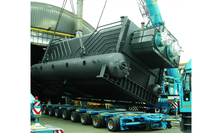 Une grande chaudière industrielle à tubes d'eau est soulevée par une grue pour être transportée.