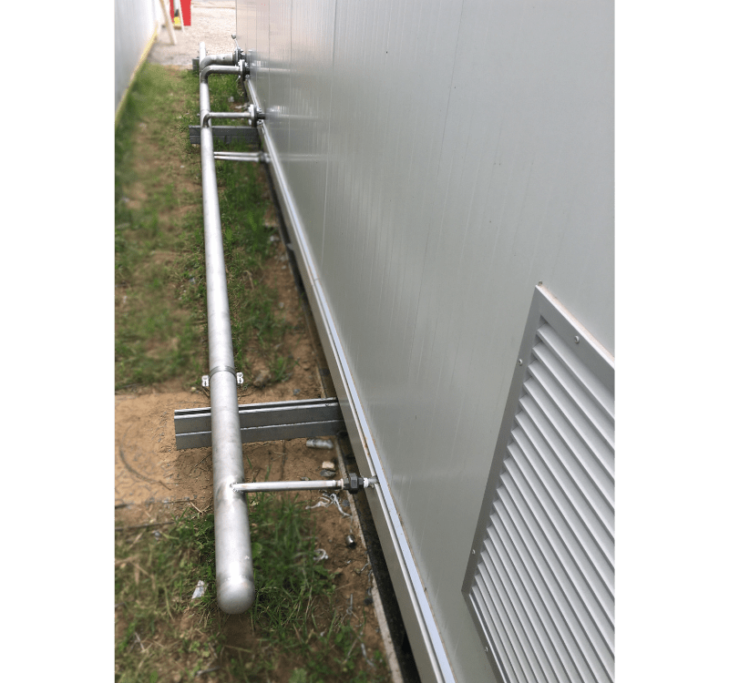 Un long tuyau métallique horizontal, un collecteur de distribution de vapeur, fixé le long d'une paroi extérieure de bâtiment, avec des raccordements.